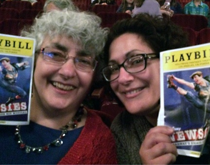 Two women smiling and holding Playbill programs for the musical 'Newsies' while sitting in a theater.