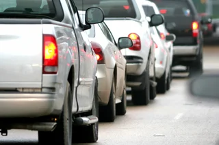 A row of cars in traffic, mostly white vehicles, showing congestion on the road.